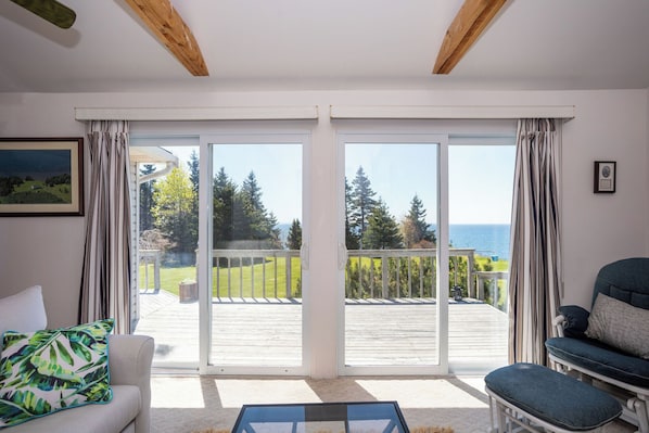 Una habitación con un amplio ventanal corredera que da a una terraza con vistas al mar y árboles.