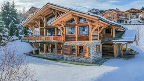 Ein mehrstöckiges Holzchalet mit großen Fenstern und einem Balkon, umgeben von Schnee.