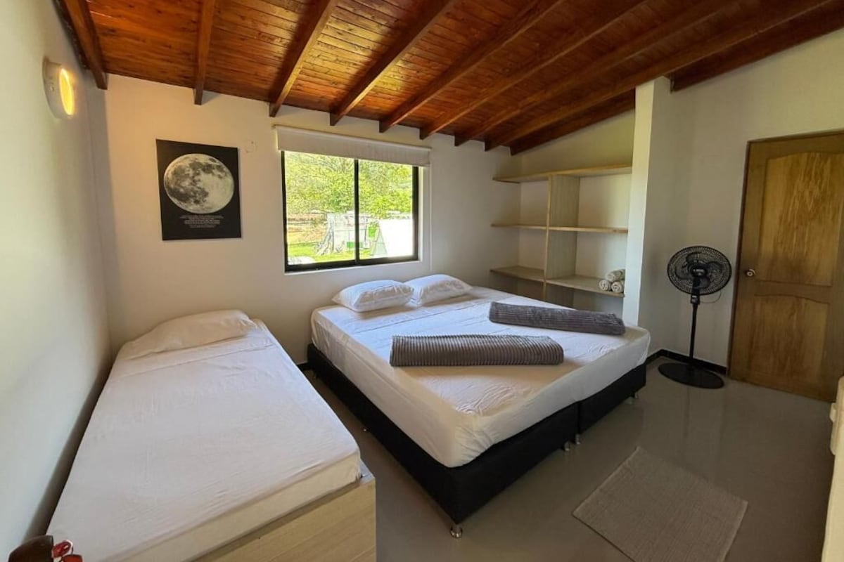 Un dormitorio con una cama, una cama individual, una ventana, un ventilador y una puerta.