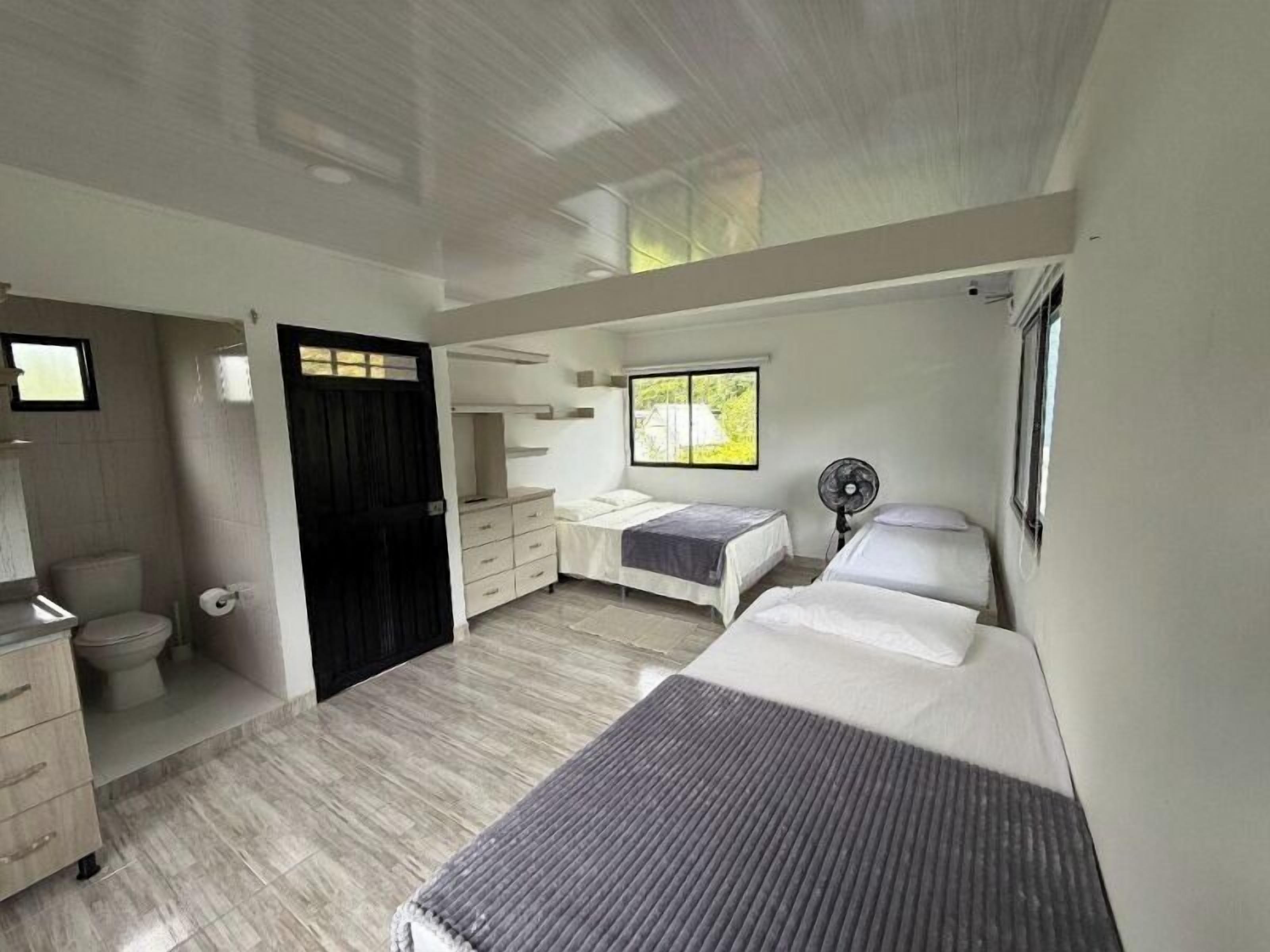 Ein Schlafzimmer mit Bett, Kommode, Ventilator und Fenster.