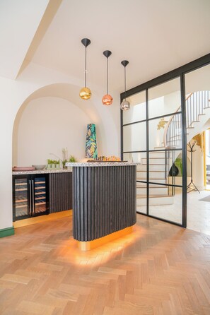 A modern kitchen with a central island, pendant lights, and a staircase leading to an upper level. - Chic Devon Designer Oasis with hot tub (Kingsbridge)