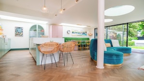 A modern kitchen with a dining area, a sofa, and a view of greenery outside. - Chic Devon Designer Oasis with hot tub (Kingsbridge)