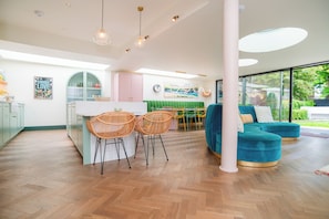 A modern kitchen with a dining area, a sofa, and a view of greenery outside. - Chic Devon Designer Oasis with hot tub (Kingsbridge)