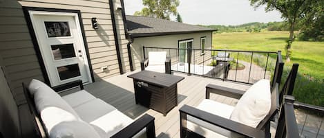 A deck with two lounge chairs and a table, overlooking a grassy field.