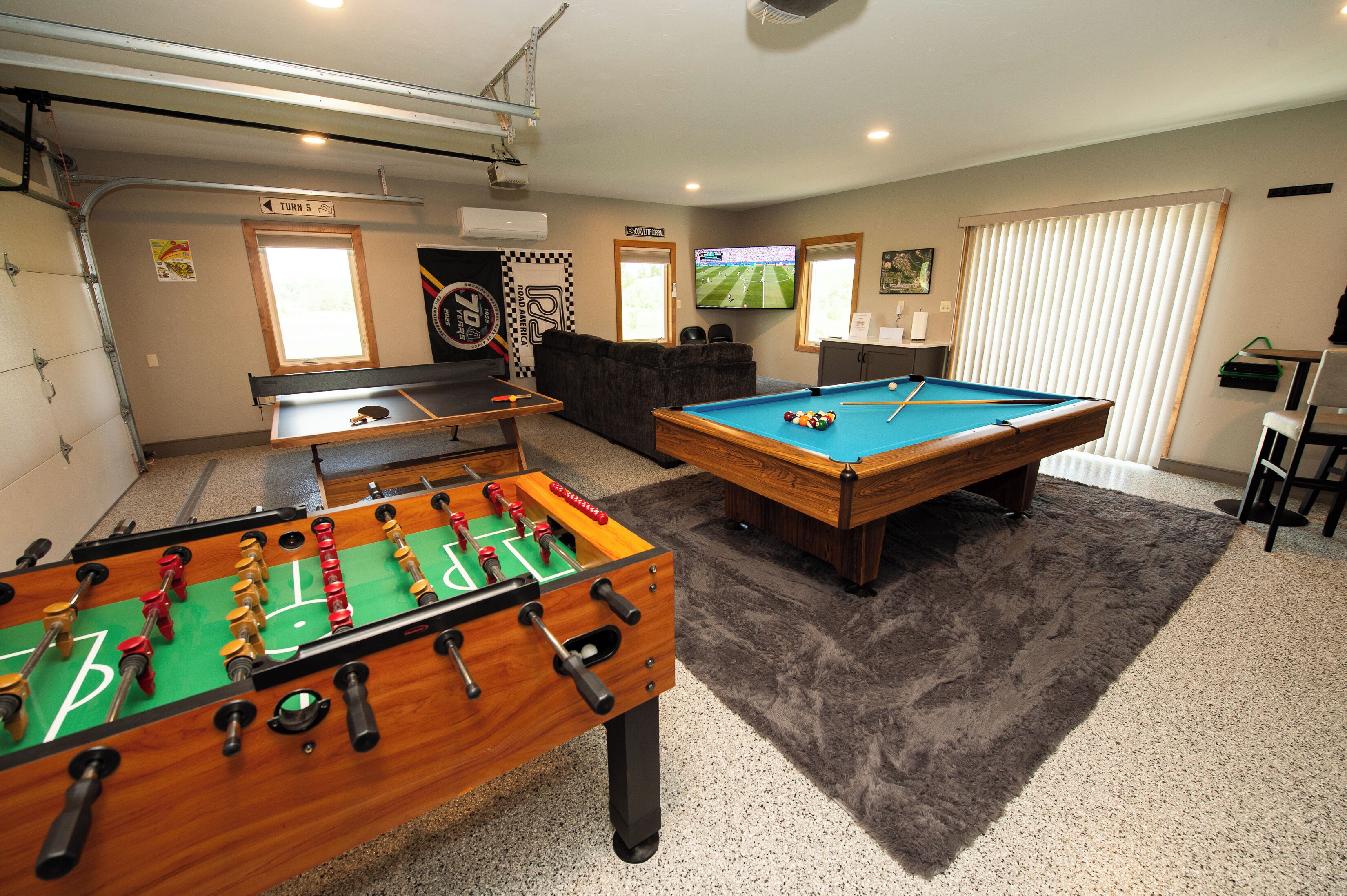 A room with a foosball table, a pool table, a television, and a seating area.