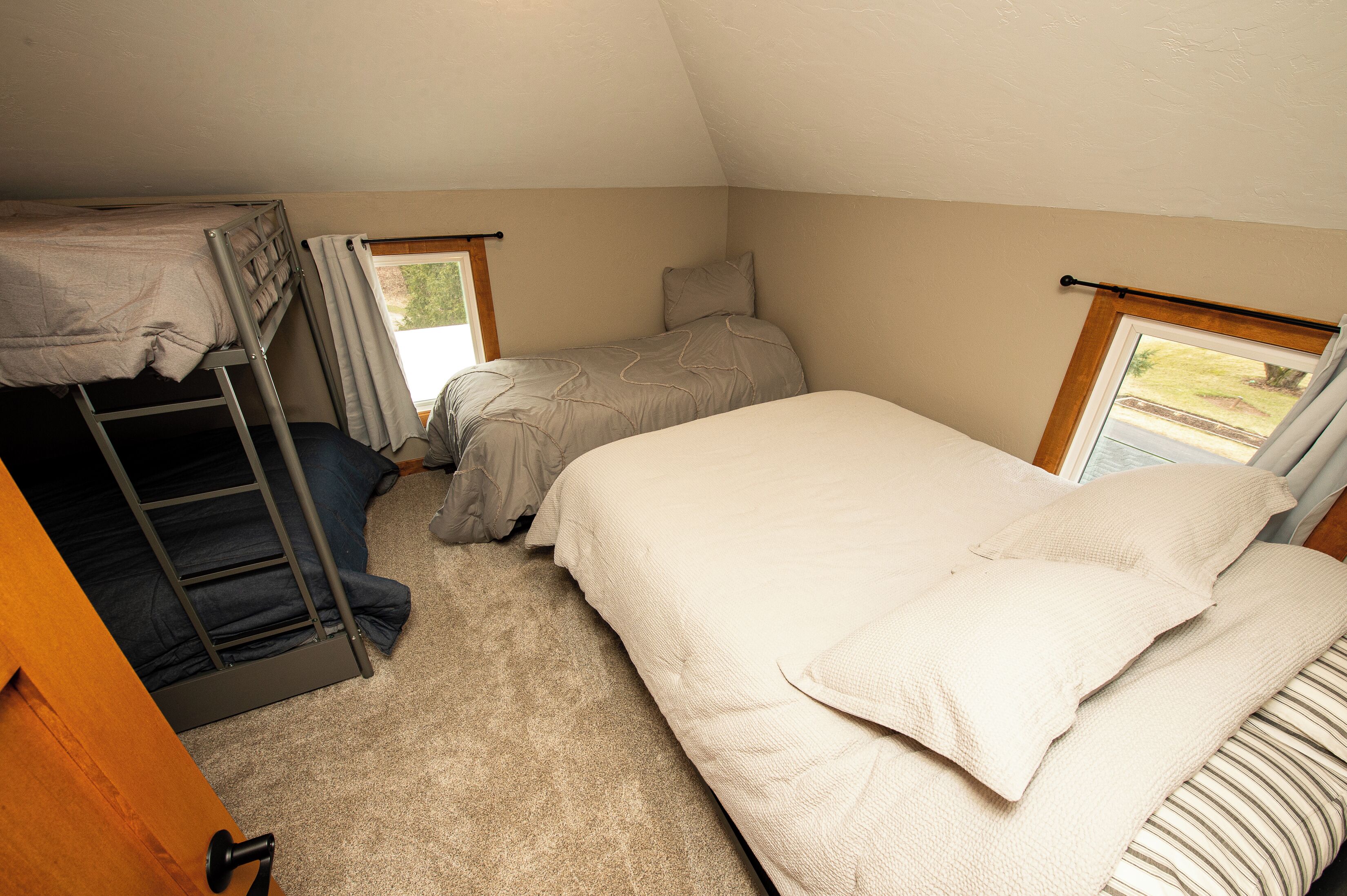 A dorm-style room with bunk beds, a single bed, and a window with curtains.