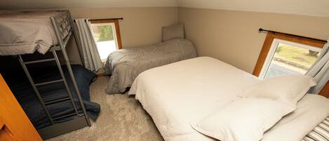 A dorm-style room with bunk beds, a single bed, and a window with curtains.