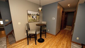 Una habitación con piso de madera, una mesa redonda con dos sillas, una lámpara colgante y un cuadro en la pared.