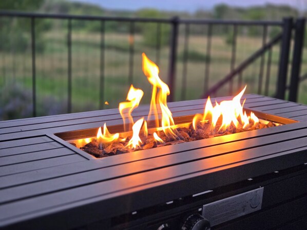 A metal fire pit with flames, surrounded by a wooden deck.