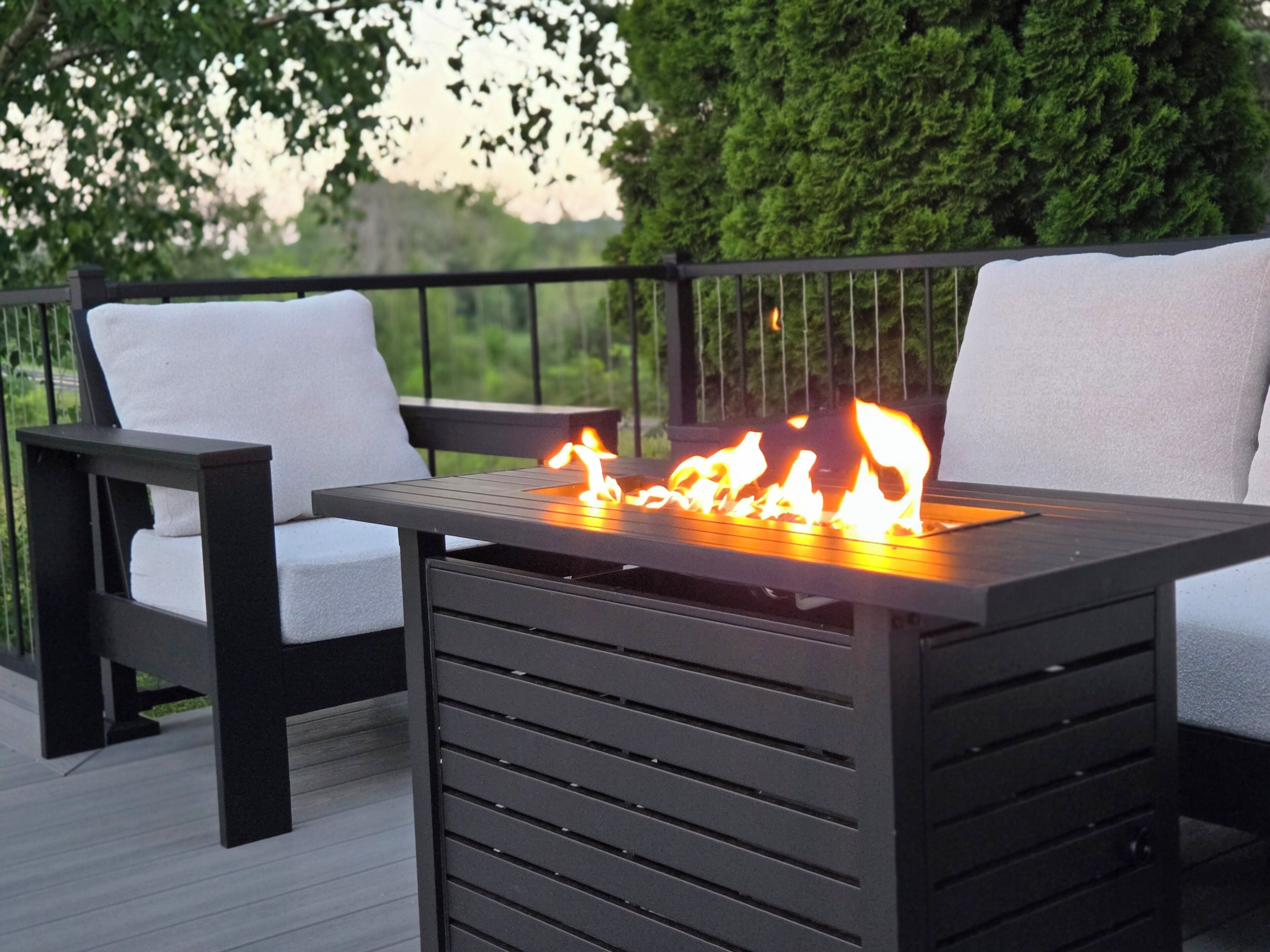 A deck with a table and chairs, a fire feature, and a railing.
