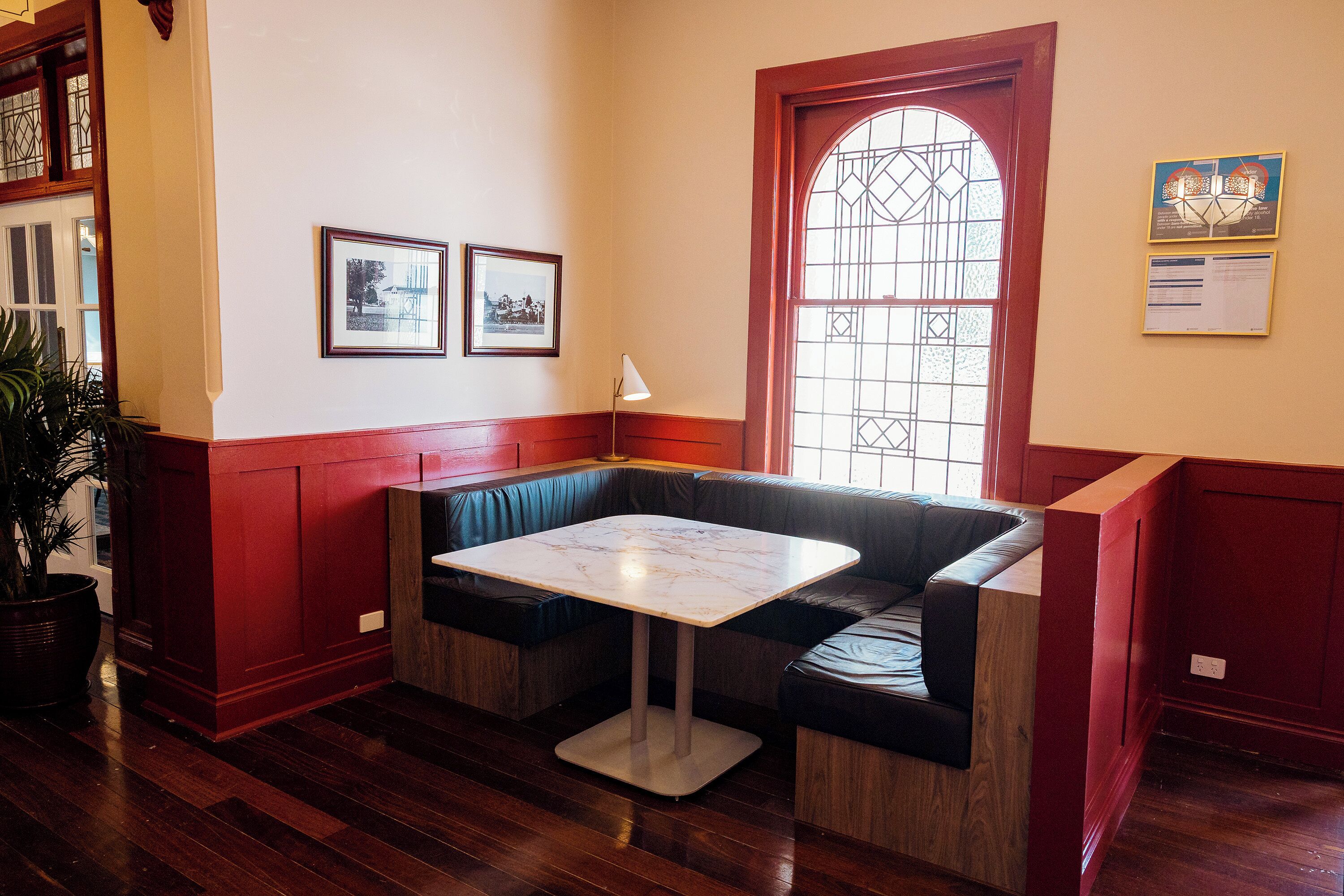 A room with a wooden floor, a red and white wall, a bench with a table, and a window with a decorative glass design.