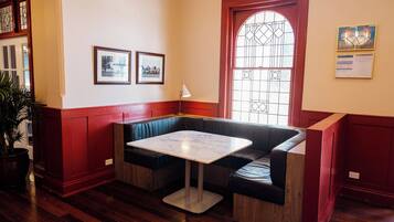 A room with a wooden floor, a red and white wall, a bench with a table, and a window with a decorative glass design.