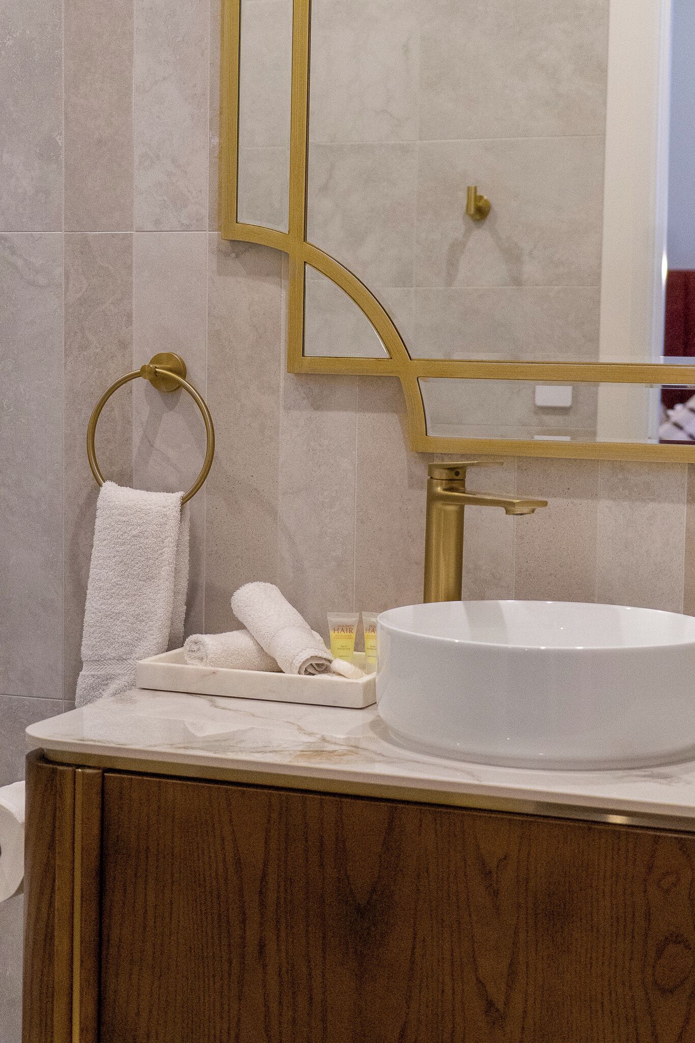 Un baño con un lavabo blanco redondo, un toallero dorado y un espejo con marco dorado.