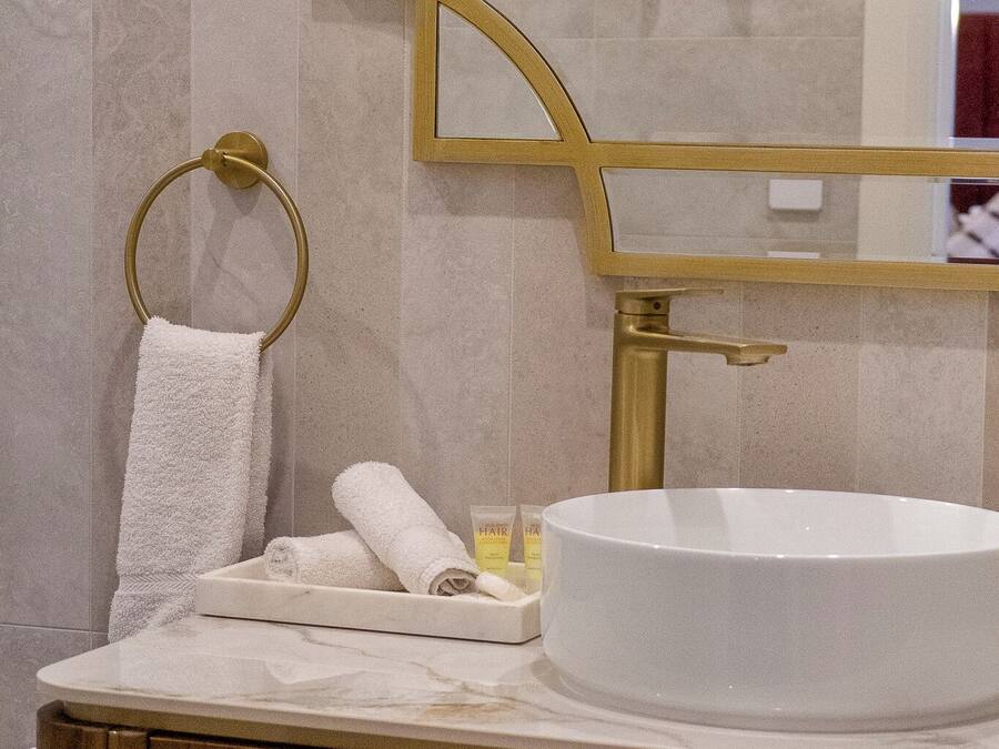 Un baño con un lavabo blanco redondo, un toallero dorado y un espejo con marco dorado.