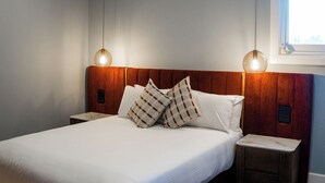 A neatly made bed with white linens and plaid pillows, a wooden headboard, and two bedside tables with lamps.