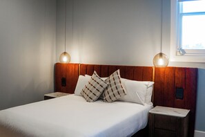 A neatly made bed with white linens and plaid pillows, a wooden headboard, and two bedside tables with lamps. - Kincraig Hotel (Naracoorte)