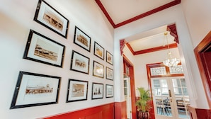 A hallway with framed historical photographs on the wall, a red wainscoting, and a staircase leading to a dining area.