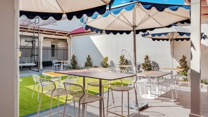 An outdoor patio with tables and chairs, umbrellas, and a small lawn area.