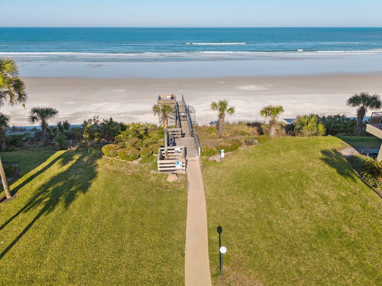A pathway leading to a beach with a deck area and palm trees.