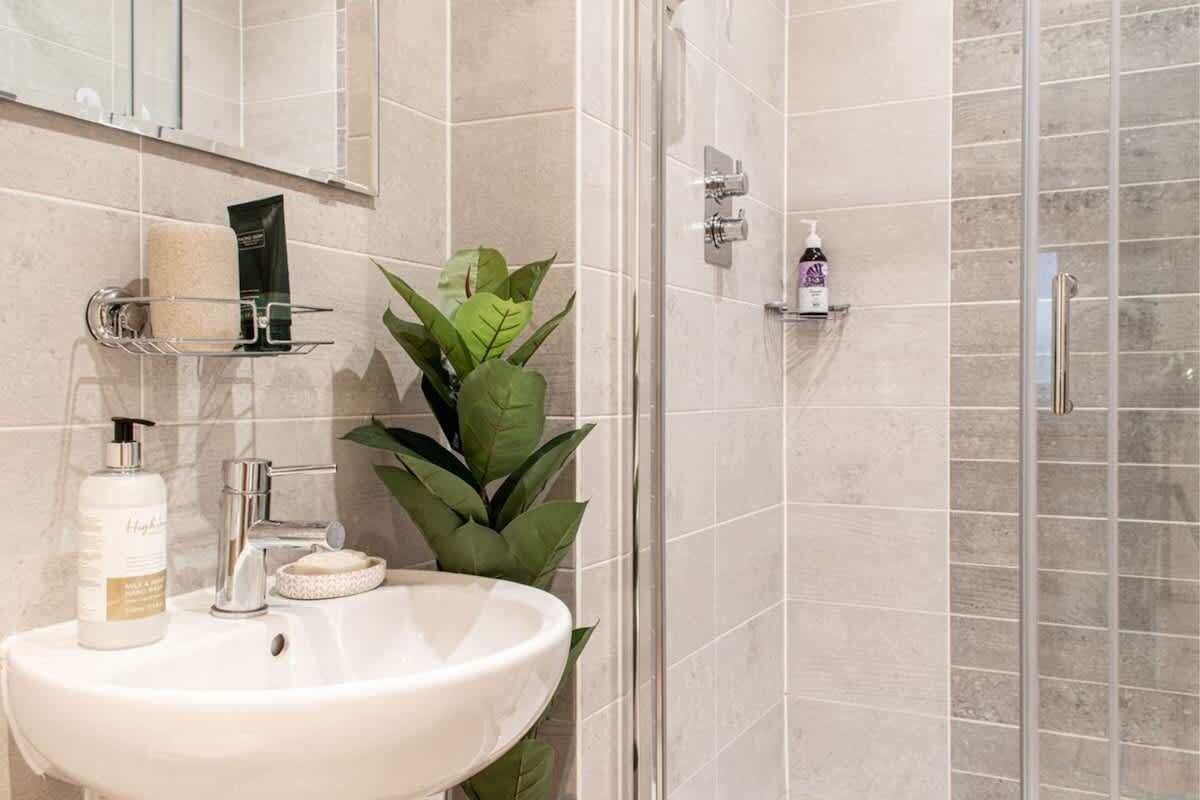 A bathroom with a sink, mirror, shower, and toiletries.