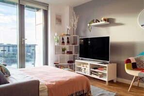 Een moderne woonkamer met een grote televisie, een boekenkast en uitzicht door een schuifdeur.