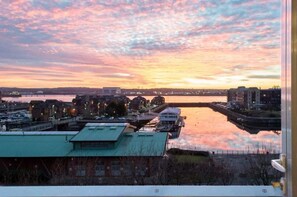 Een uitzicht op het water met gebouwen, een brug en een rustig wateroppervlak tijdens de zonsondergang.