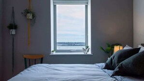 A bedroom with a bed, a window, and a view of a cityscape. - Modern 2BR Apartment w/ Balcony | Sleeps 6 (Merseyside)