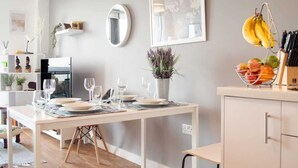 A dining area with a white table set for four, a mirror, a framed picture, and a fruit basket. - Modern 2BR Apartment w/ Balcony | Sleeps 6 (Merseyside)