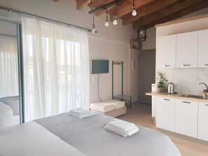 Una habitación de hotel moderna con cama, televisión, un pequeño rincón de descanso, kitchenette y baño.