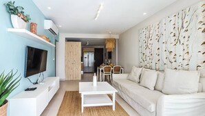 Ein modernes Wohnzimmer mit Flachbildfernseher, weißem Sofa und Essbereich mit Stühlen und Tisch.
