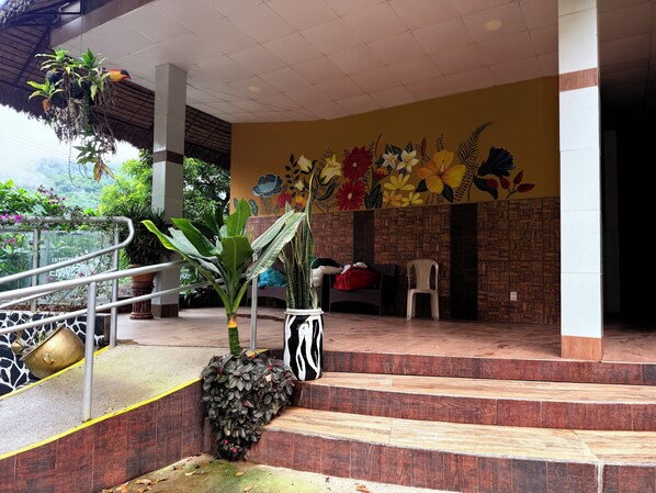 Fachada de hotel con escaleras, un mural y plantas en macetas.