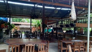 Un restaurante al aire libre con mesas y sillas de madera, una zona de estar cubierta y una barra.