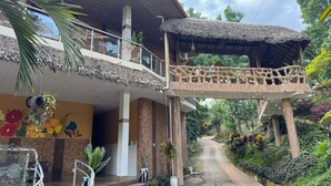 Un hotel con balcón cubierto, escalones que conducen a la entrada y un camino de jardín.