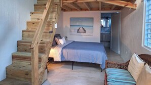 Ein Schlafzimmer mit einer Holztreppe, einem Bett, einem Korbstuhl und einem durch eine offene Tür erreichbaren Badezimmer.