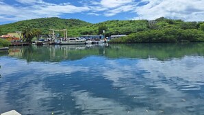 Ein ruhiger Fluss mit angestaubten Booten, eine Anlegestelle mit einem kleinen Gebäude und üppige, grüne Hügel im Hintergrund.
