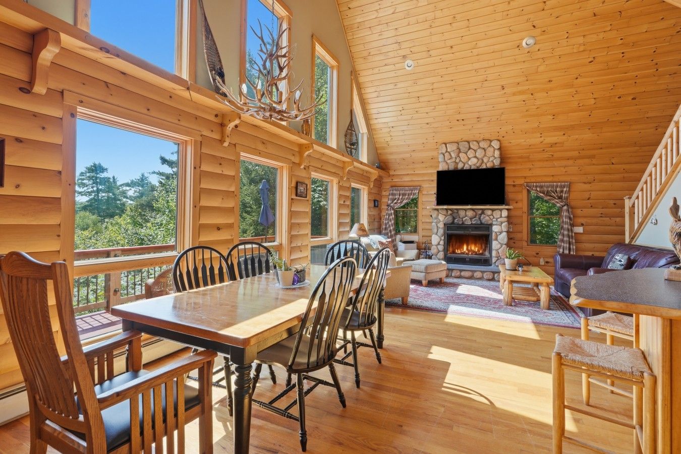 L’intérieur d’une cabane en rondins comprend un coin repas, un salon, une cheminée et de grandes fenêtres.