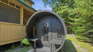 Una estructura cilíndrica con puerta y ventanas, ubicada en un área verde con un edificio al fondo.