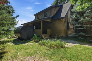A log cabin with a porch, a large barrel, and a forested backdrop. - Lake View House with Hot Tub, Sauna and Game Loft (Woodstock)