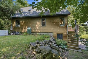A log cabin with a stone wall, a wooden deck, and a Generac generator. - Lake View House with Hot Tub, Sauna and Game Loft (Woodstock)