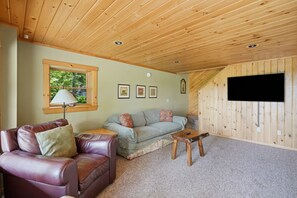 A cozy room with a leather armchair, a sofa, a small wooden table, and a TV mounted on a wooden wall.