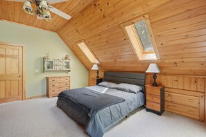 A bedroom with a sloped ceiling, a bed with grey bedding, two bedside tables with lamps, a dresser, and a wall-mounted cabinet. - Lake View House with Hot Tub, Sauna and Game Loft (Woodstock)