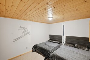 A bedroom with two beds, a wooden ceiling, and a ski-themed wall decoration.