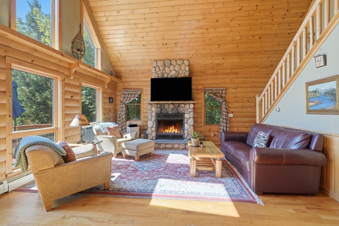 L'intérieur d'une cabane en rondins, avec une cheminée, des meubles en bois et de grandes fenêtres.