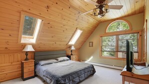 Un dormitorio con una cama, mesitas de noche, un escritorio, un televisor y un ventilador de techo.
