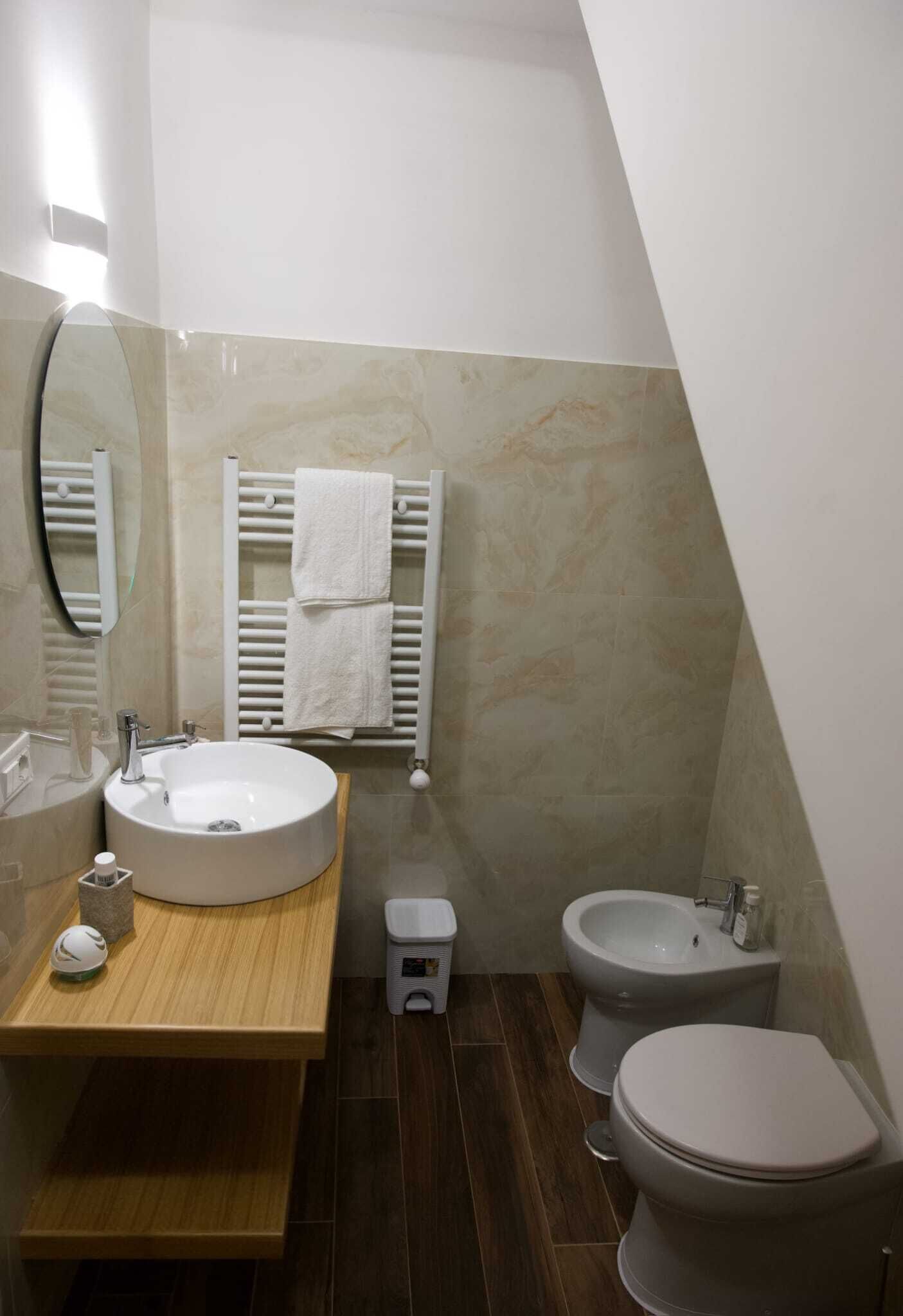 A bathroom with a round sink, a mirror, a towel rack, a bidet, and a toilet.