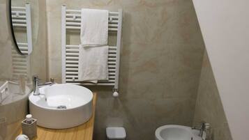 A bathroom with a round sink, a mirror, a towel rack, a bidet, and a toilet.