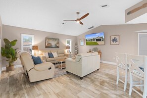 A spacious living room with a ceiling fan, a large flat-screen TV, and a dining area with white chairs. - 2BR2BATH Venice Poolside Retreat (Venice)
