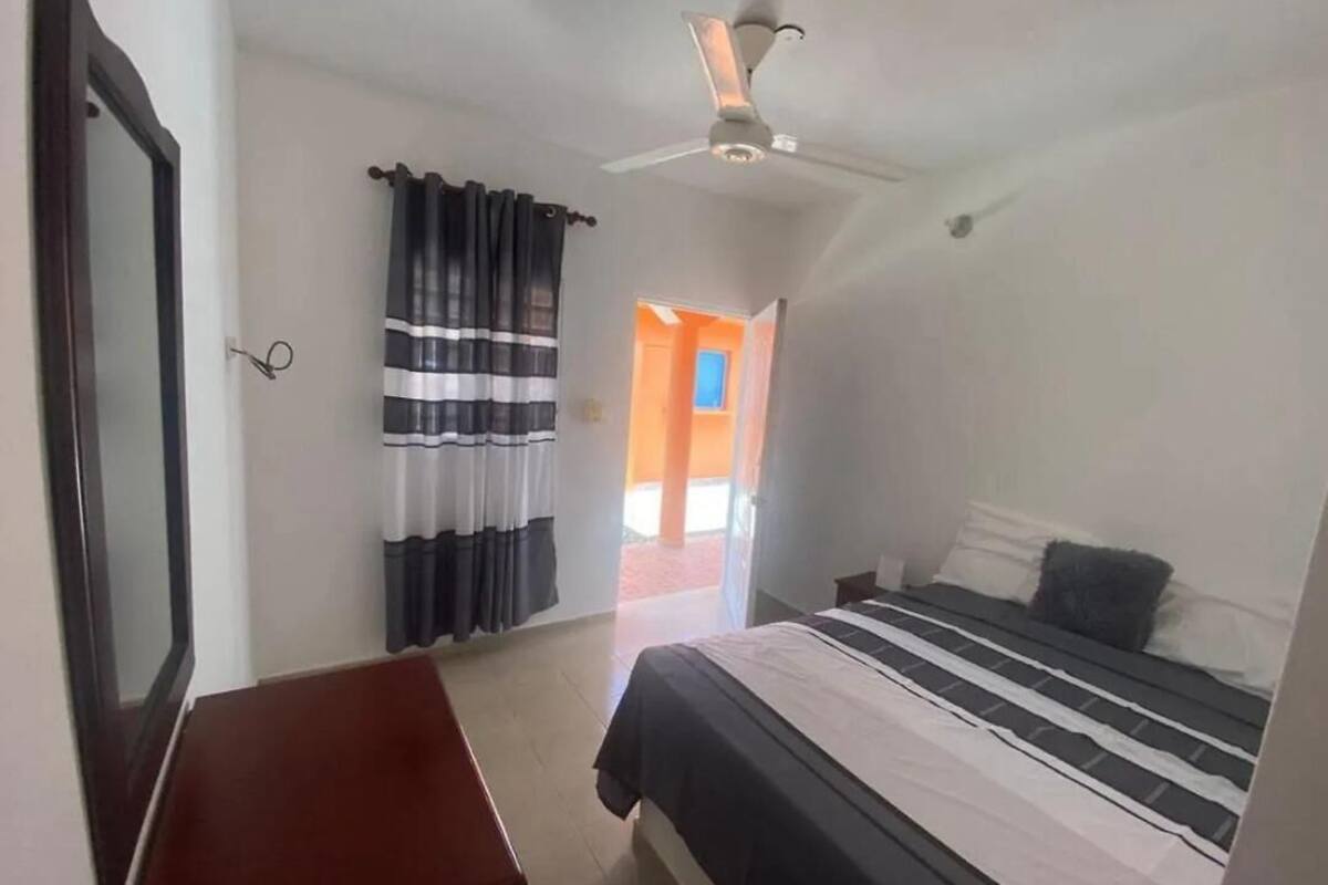 Une chambre à coucher avec un lit, un ventilateur de plafond, une fenêtre avec des rideaux et une porte.