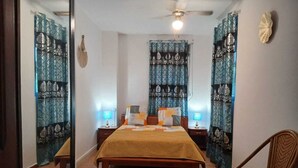 A bedroom with a bed, bedside tables, a chair, and patterned curtains. - MAGNIFICENT FURNISHED VILLA WITH SWIMMING POOL AND MOUNTAIN VIEW (Petit-Bourg)