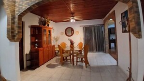 A dining area with a brick archway, a ceiling fan, a dining table with chairs, a cabinet, and a mirror on the wall. - MAGNIFICENT FURNISHED VILLA WITH SWIMMING POOL AND MOUNTAIN VIEW (Petit-Bourg)